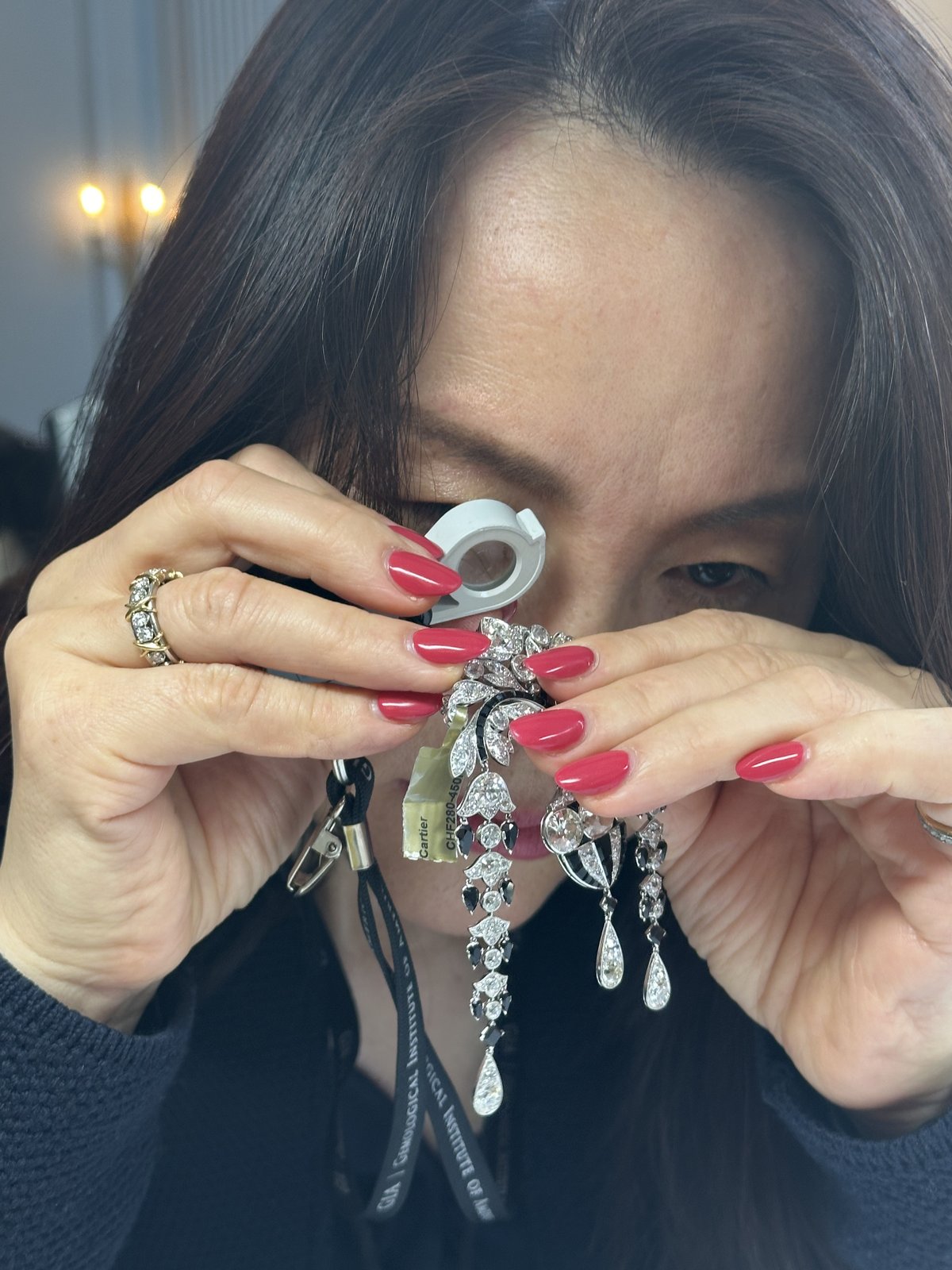 Close-up of Kehan Li examining a pair of long diamond pendant earrings down a loupe at a Geneva auction preview.